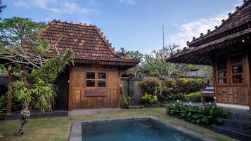 Una casa de madera tradicional con techo de tejas, piscina y abundante vegetación.