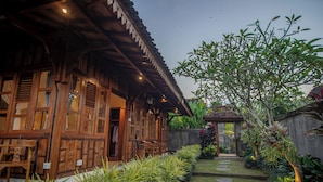 A traditional wooden house with a covered porch, a stone pathway, and lush greenery. - Kerjim Wooden Villa (Sukawati)