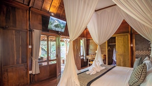 A room with a bed, canopy, wooden walls, a television, and a view of greenery outside. - Kerjim Wooden Villa (Sukawati)