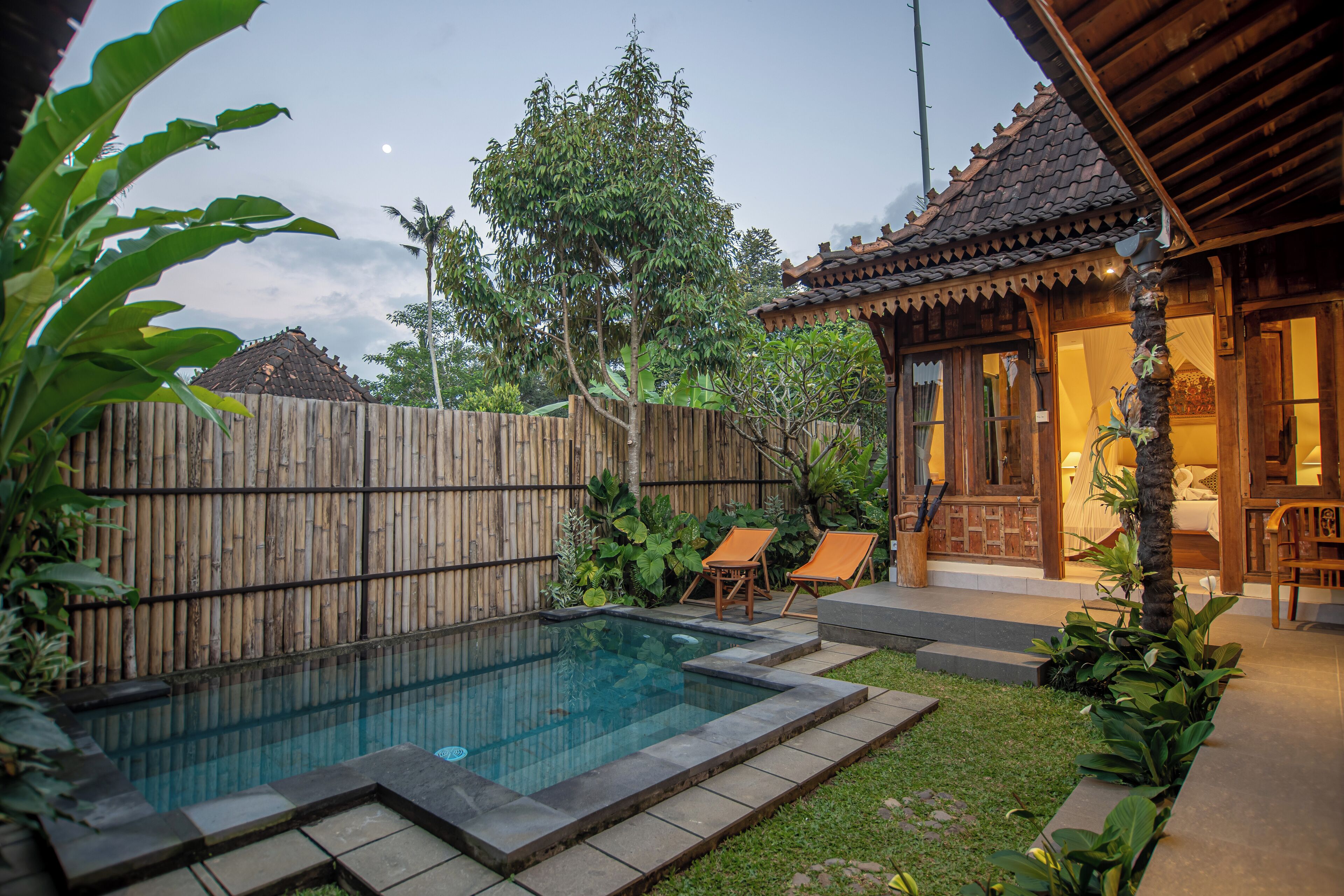 A backyard with a swimming pool, wooden deck, and a small building with a tiled roof.