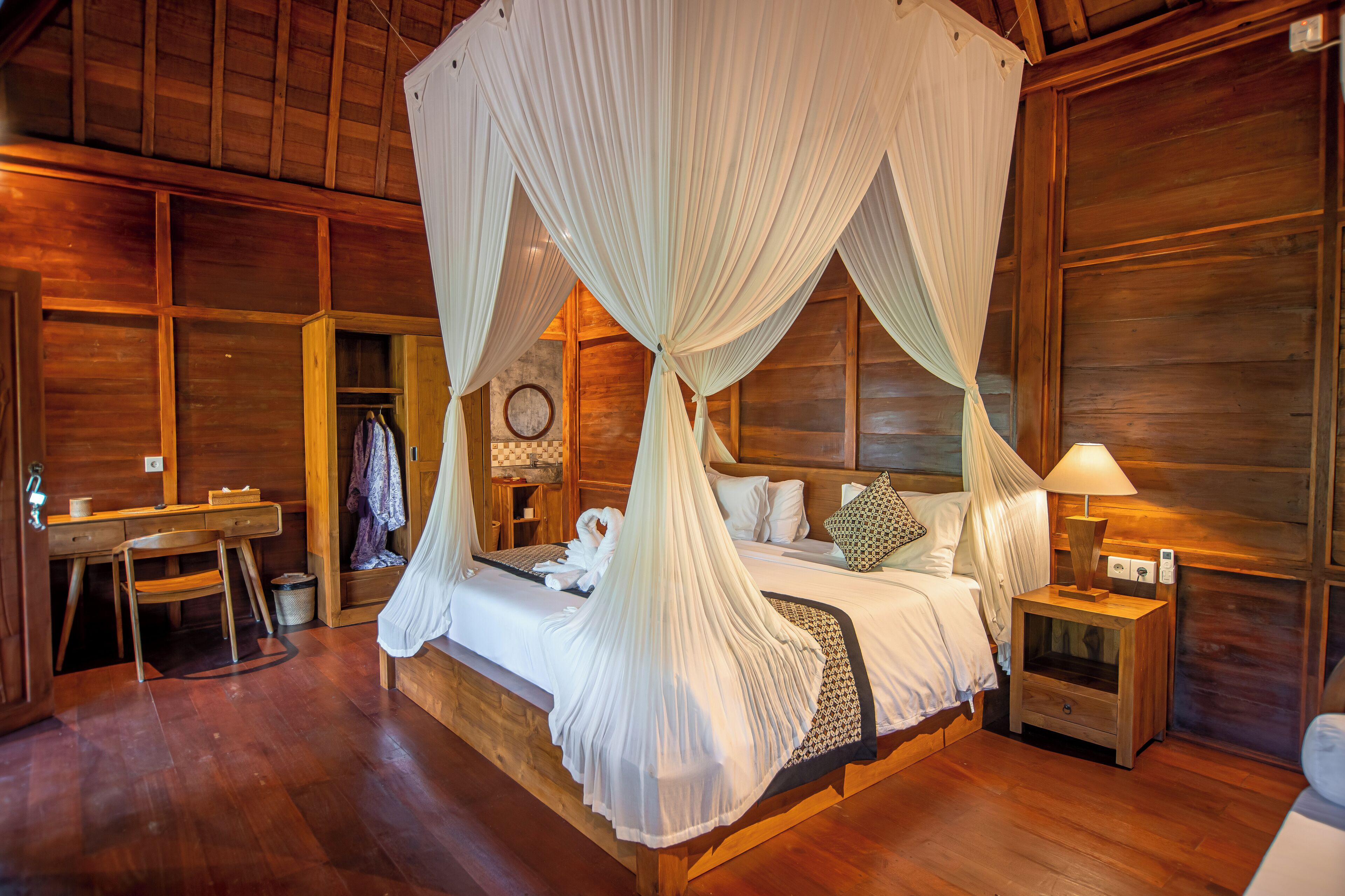 Un dormitorio de cabaña de madera con una cama con dosel, un escritorio de madera y una mesita de noche con una lámpara.