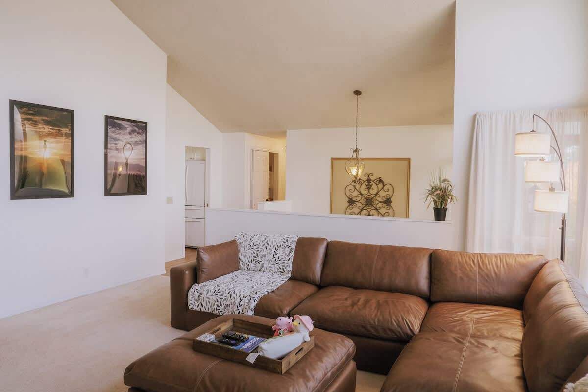 Een woonkamer met een bruine leren bank, een salontafel met boeken en een speeltje, en twee ingelijste foto's aan de muur.