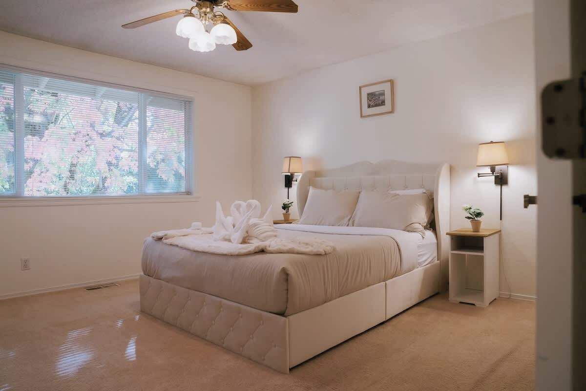 Un dormitorio con una cama grande, dos mesitas de noche con lámparas, un ventilador de techo y una ventana con persianas.