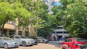 A parking lot with several cars, including a red Tesla, and a building with a gated entrance in the background. - Tyms Xujiahui Premium 3BR 2BA APT  (Shanghai)