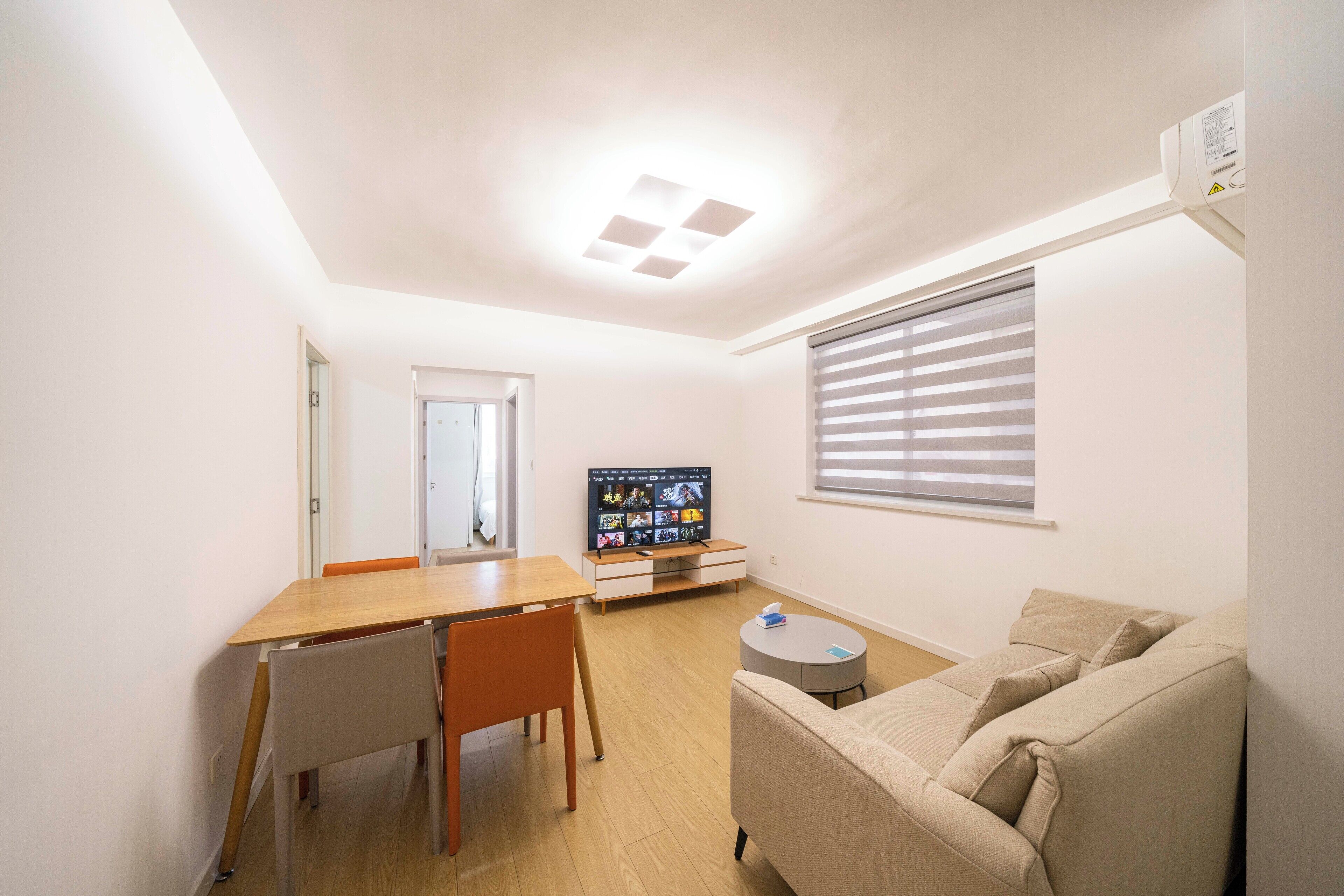 A compact living space with a dining area, a sofa, a TV, and a window with blinds.