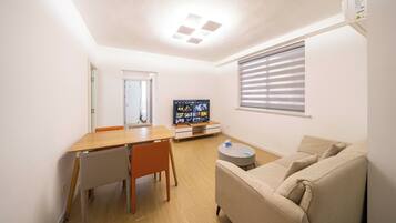 A compact living space with a dining area, a sofa, a TV, and a window with blinds.