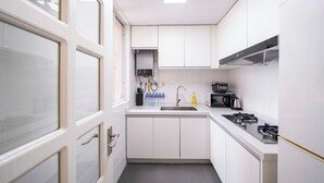 A compact kitchen with white cabinets, a gas stove, a microwave, and a sink. - Tyms Xujiahui Premium 3BR 2BA APT  (Shanghai)