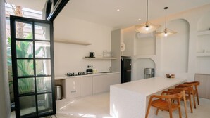 A modern kitchen with a large island, wooden chairs, and a hanging light fixture. - SOOJIWA VILLA by Taman Bali (Canggu)