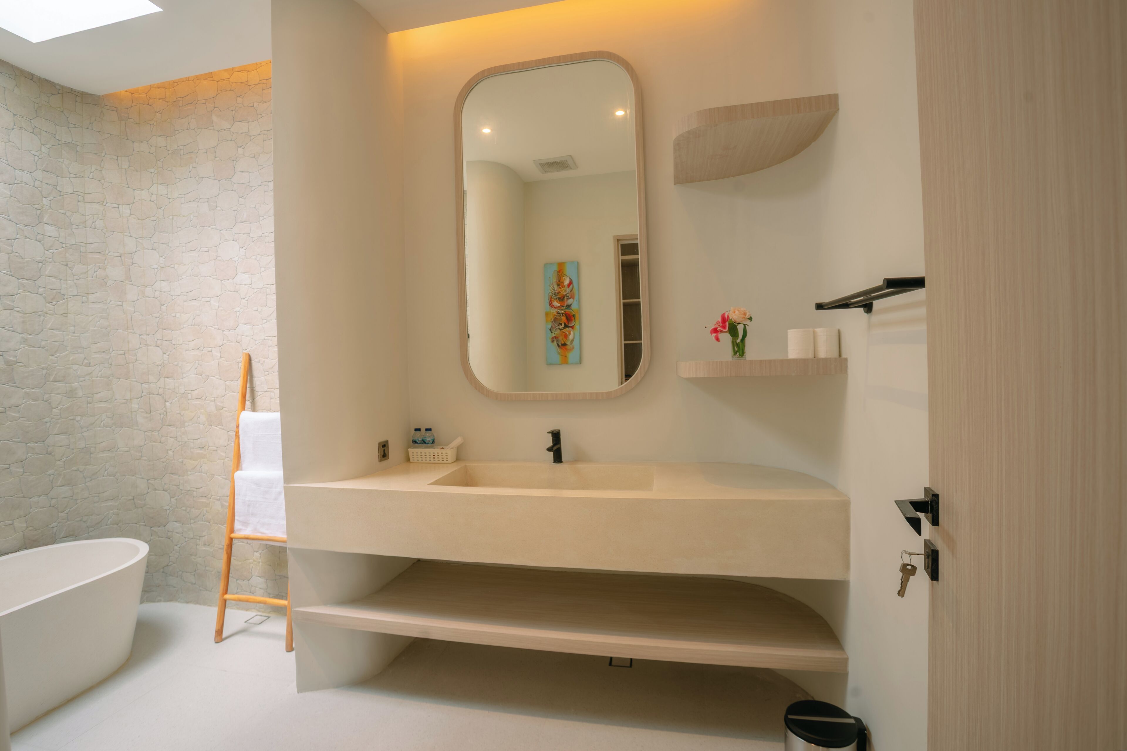 Un baño moderno con una bañera independiente, un espejo grande y un mueble de tocador de madera.