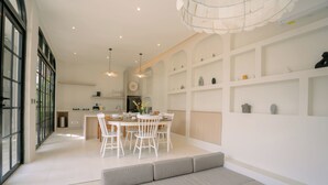 A modern kitchen with white cabinetry, a dining area with a round table and chairs, and a built-in bench. - SOOJIWA VILLA by Taman Bali (Canggu)