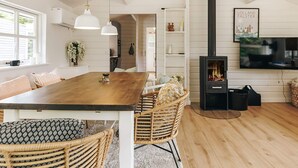 Ein geräumiger Wohnbereich mit einem Holzessttisch, Korbstühlen, einem Kamin und einem an der Wand befestigten Fernseher.