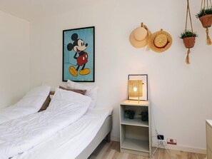 A bedroom with a bed, a wall-mounted Mickey Mouse painting, a bedside lamp, and two hanging planters. - 4 Star Holiday Home in Vaeggerlose (Vaeggerlose)