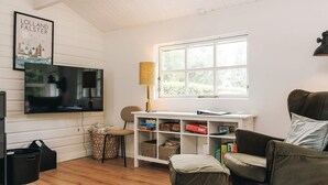 Ein gemütliches Wohnzimmer mit Fernseher, Lampe, Bücherregal und einem Fenster mit Blick auf Grünflächen.