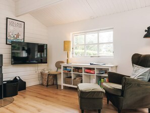 A cozy living room with a television, a lamp, a bookshelf, and a window with a view of greenery. - 4 Star Holiday Home in Vaeggerlose (Vaeggerlose)