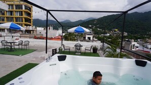 Una vasca idromassaggio su un terrazzo panoramico con vista sulla città e sulle montagne.
