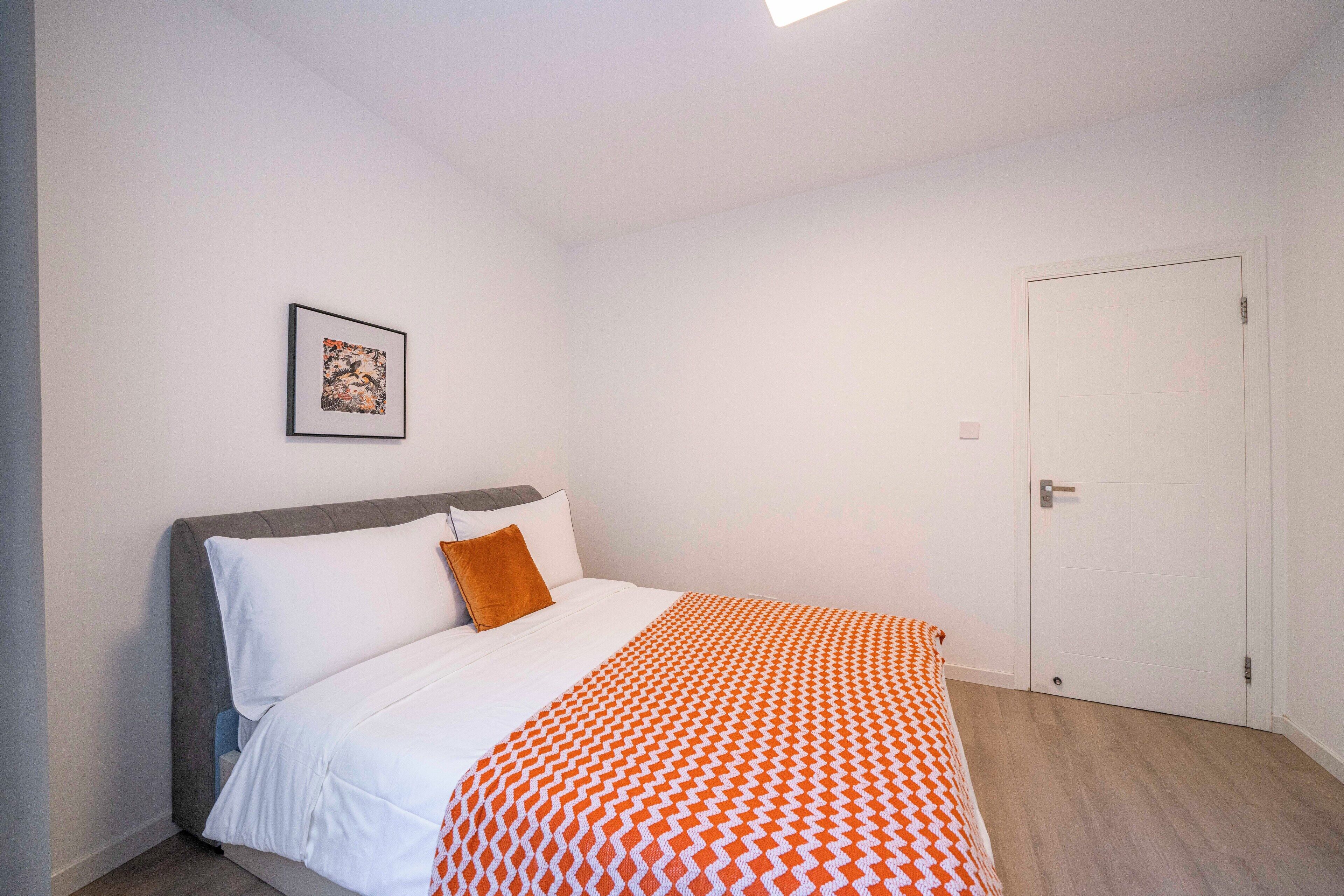 Een slaapkamer met een bed, een deur en een lijst met een afbeelding aan de muur.