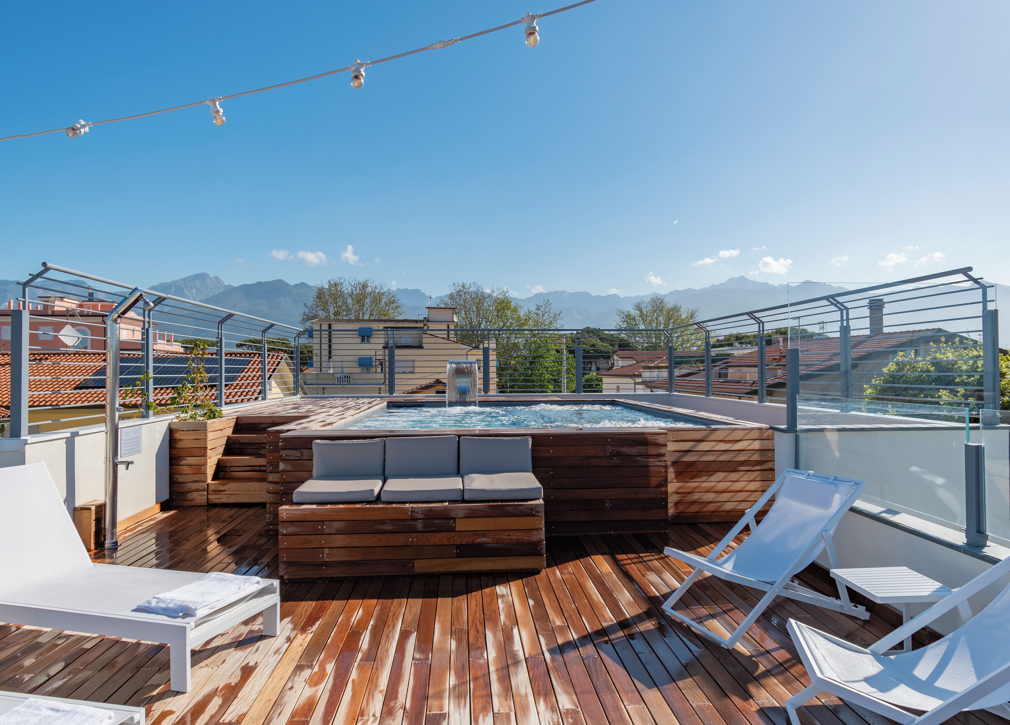 A rooftop pool area with wooden decking, lounge chairs, and a hot tub.
