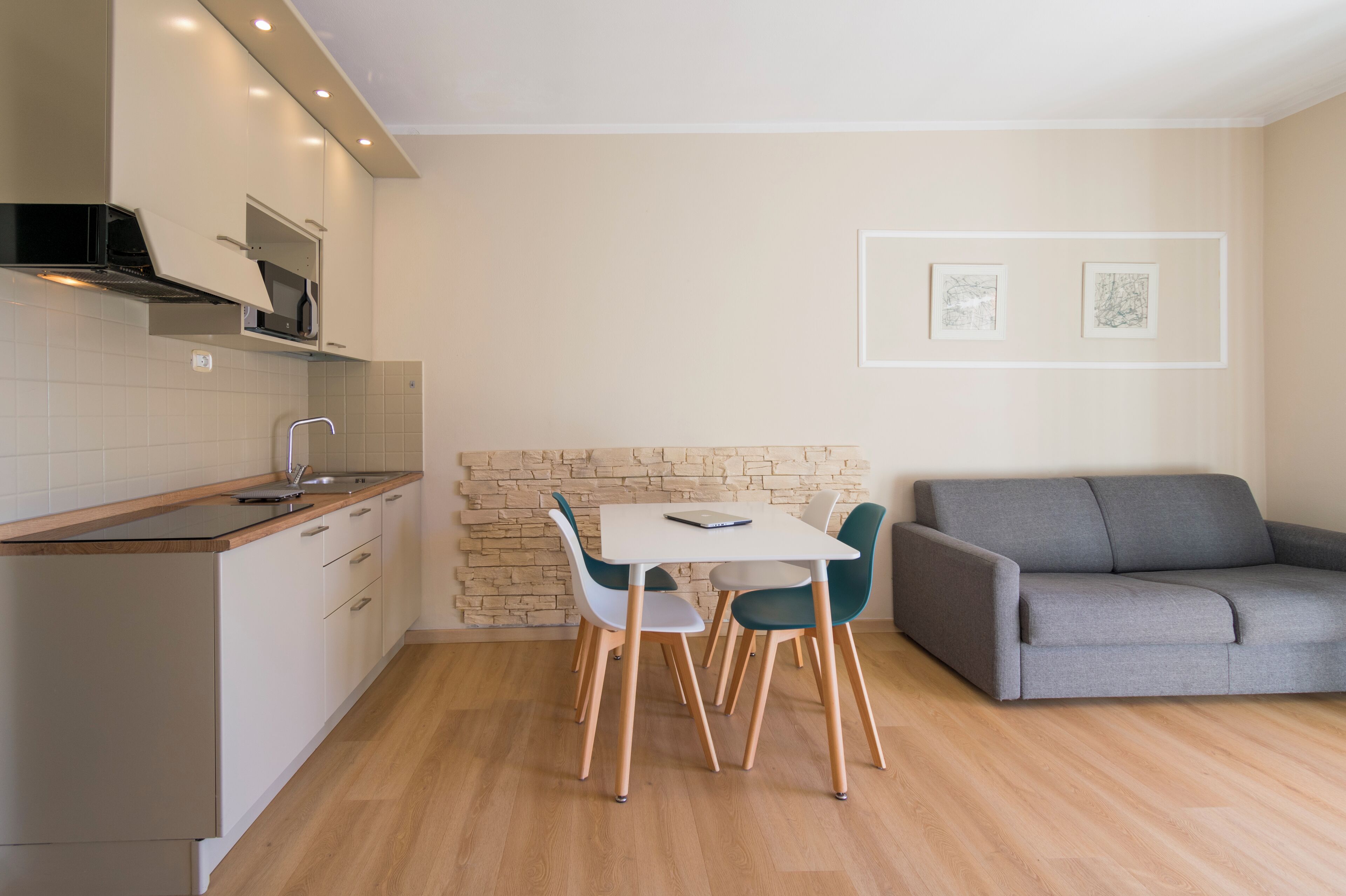 Una cocina moderna con comedor, un sofá gris y dos cuadros en la pared.