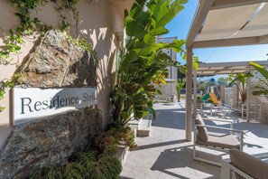 A sign reading 'Residence Stella' with a rock and greenery backdrop, outdoor seating, and a covered area with a view of the sky. - Residence Stella (Massa)
