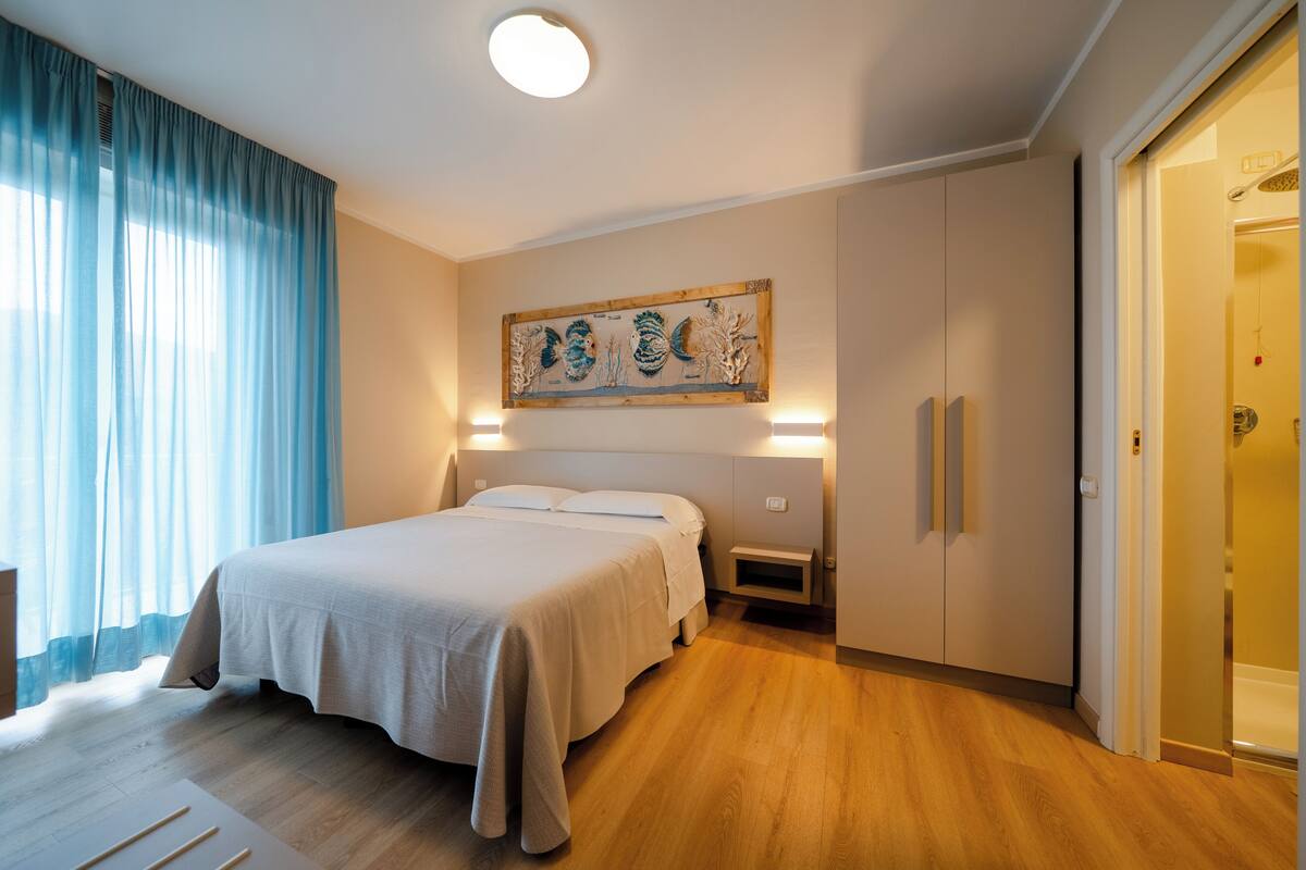 Habitación de hotel con una cama, una mesita de noche, una obra de arte colgada en la pared, un armario y una puerta que da a un baño.