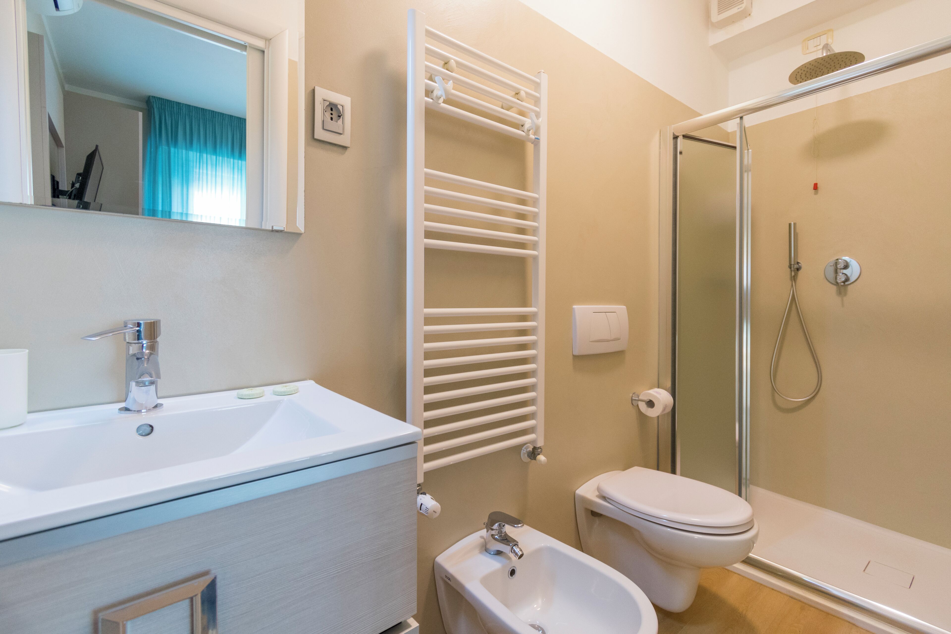 A modern bathroom with a white sink, a bidet, a toilet, and a glass-enclosed shower.