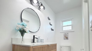Ein modernes Badezimmer mit einem Holzkonsolenunterschrank, einem runden Spiegel und einer Toilette.