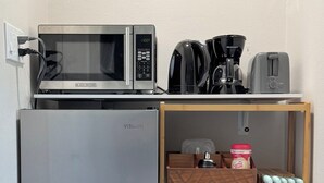 Eine kompakte Küchenzeile mit Mikrowelle, Kaffeemaschine, Toaster und einem kleinen Kühlschrank.