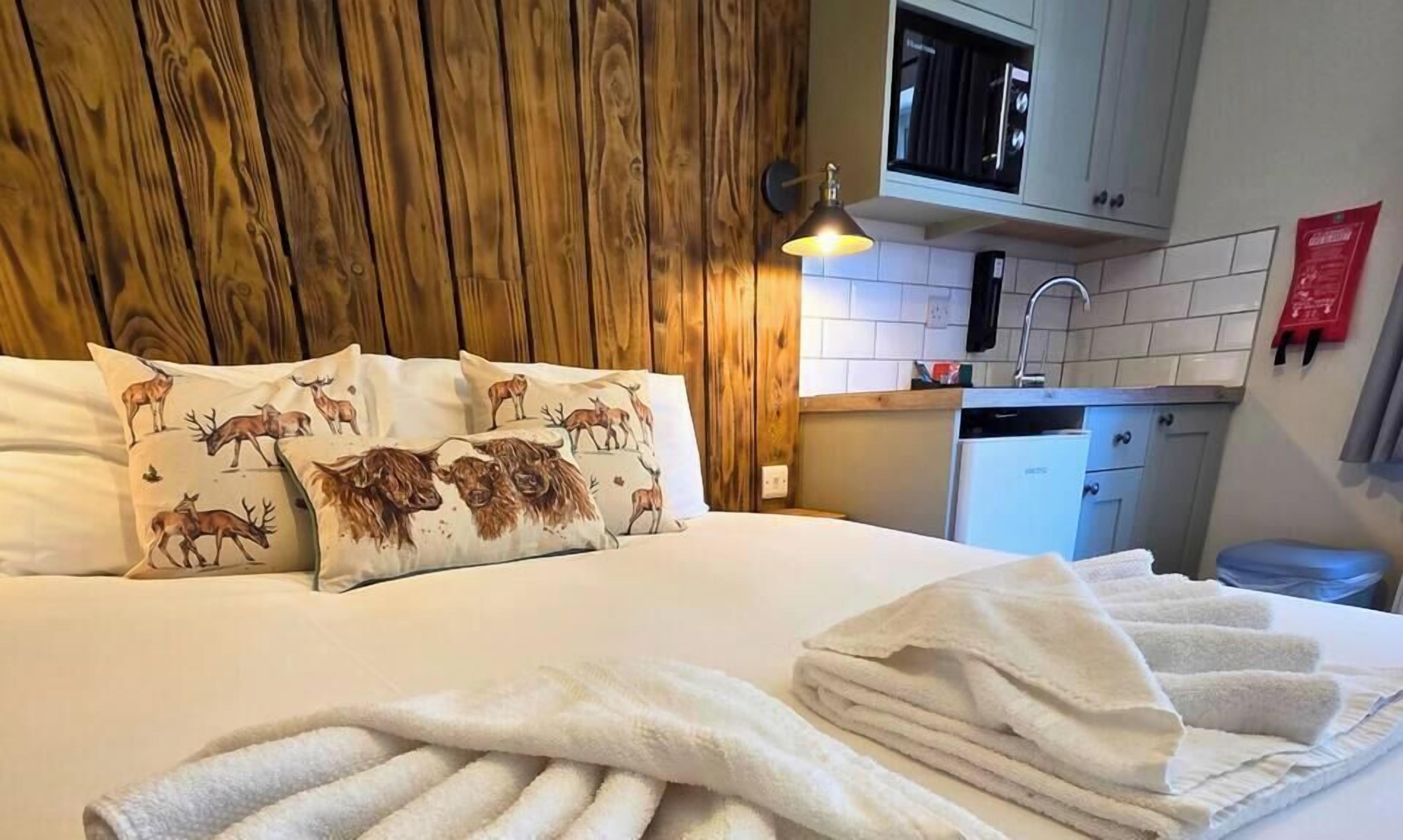 A neatly made bed with rolled white towels, a wooden headboard, and decorative pillows with animal prints.