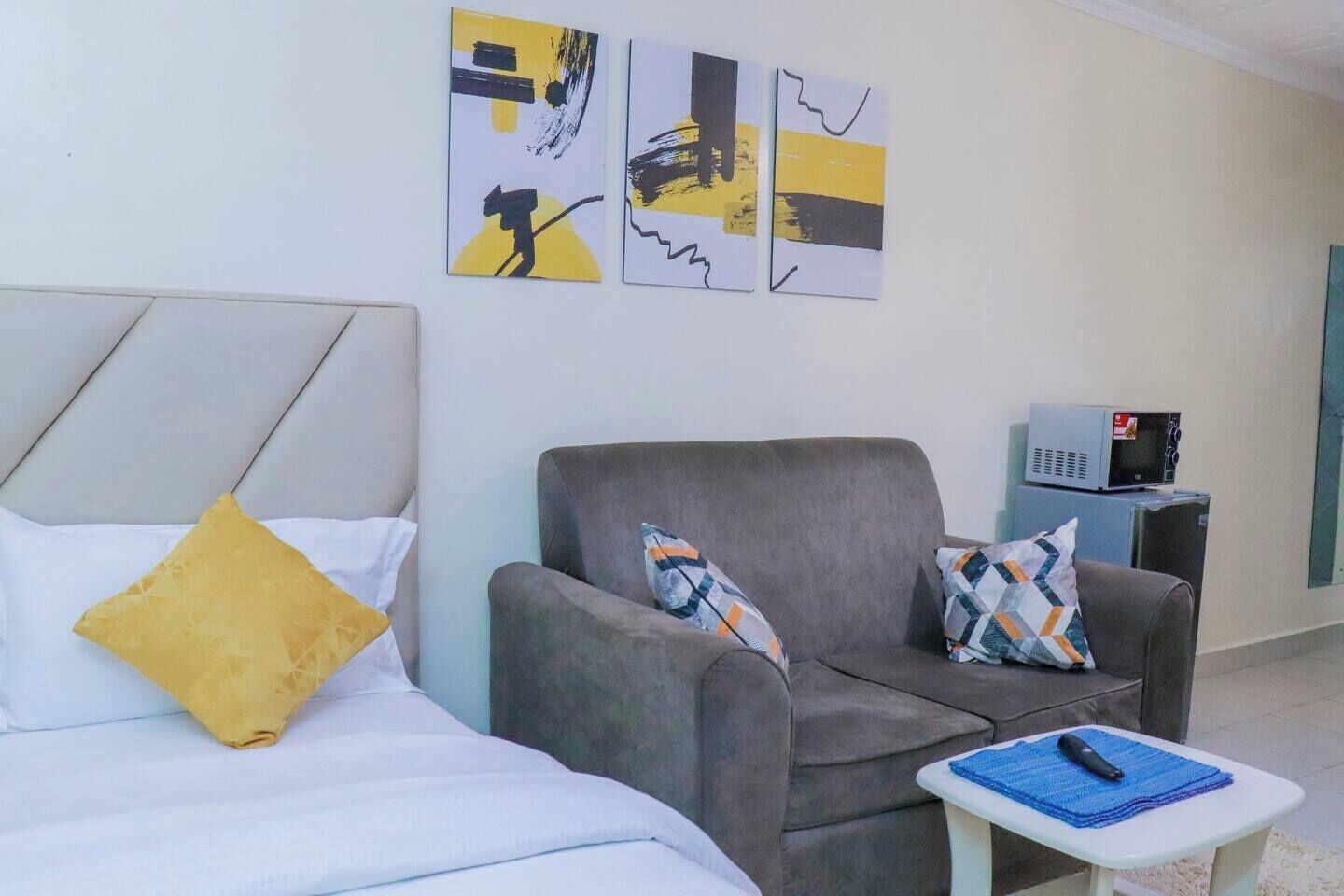 Et moderne hotelværelse med en seng, en grå lænestol og et lille bord med en fjernbetjening.