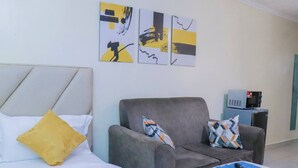 Une chambre d’hôtel moderne, équipée d’un lit, d’un fauteuil gris et d’une petite table sur laquelle se trouve une télécommande.