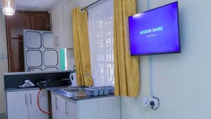A compact kitchen with a built-in stove, a sink, and a countertop. A flat-screen TV is mounted on the wall displaying 'WISDOM- SHARE Smart Cloud TV'.