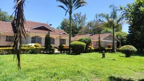 A two-story house with a tiled roof, surrounded by a well-maintained lawn and various trees.