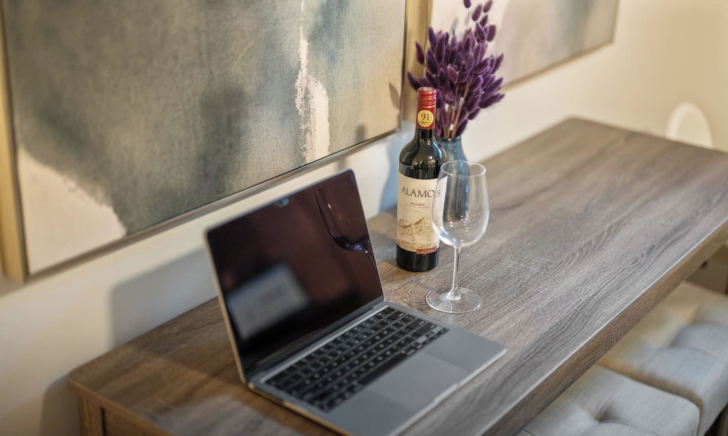 Una laptop sobre una mesa de madera, con una botella de vino y una copa.