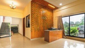 A hotel lobby with a wooden reception desk, a staircase, and a large window with a view of the outdoors. - Hill Resort Alibaug (Alibag)