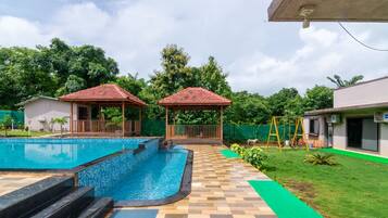 A swimming pool with two gazebos, a covered patio area, and a well-maintained lawn.