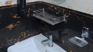 A bathroom with a white sink, a mirror, and a black and gold marble backsplash. - Hotel Prince Palace (Ayodhya)