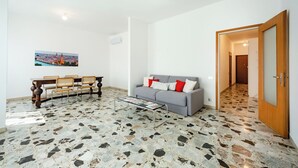 A living room with a sofa, a coffee table, a dining table with chairs, a cityscape painting, and a patterned floor. - Myarenaverona (Verona)