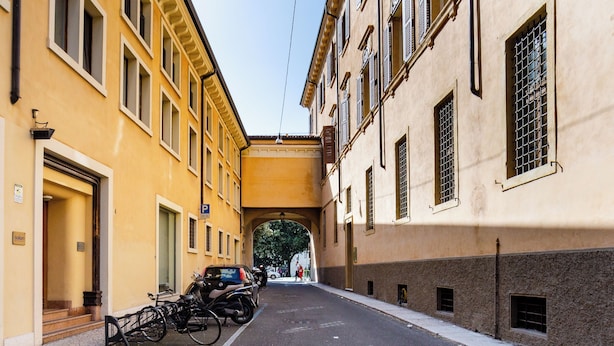 A narrow street with buildings on either side, a covered passageway, and parked bicycles. - Myarenaverona (Verona)