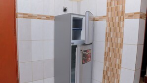 A compact refrigerator with a freezer compartment, located in a corner with tiled walls and a door to the left.