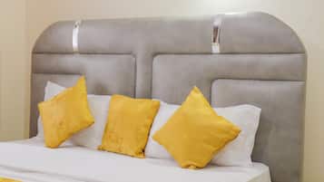 A bed with a grey upholstered headboard, white bedding, and three yellow pillows.
