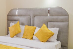 A bed with a grey upholstered headboard, white bedding, and three yellow pillows.