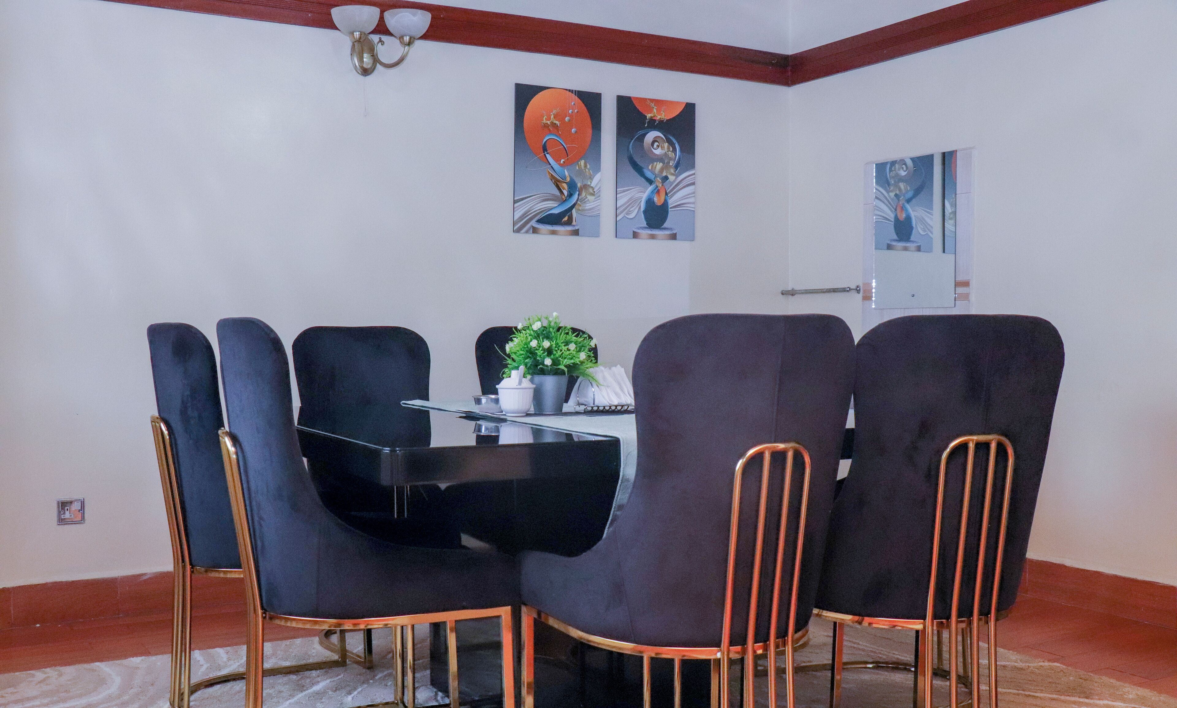 Un espace repas comprenant une table noire, quatre chaises noires aux pieds en cuivre et deux luminaires fixés au mur.