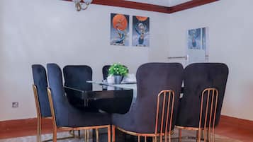 Un espace repas comprenant une table noire, quatre chaises noires aux pieds en cuivre et deux luminaires fixés au mur.