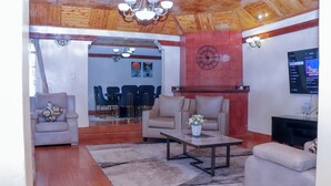 A living room with a wooden ceiling, a fireplace, a television, and a dining area with chairs and a table.