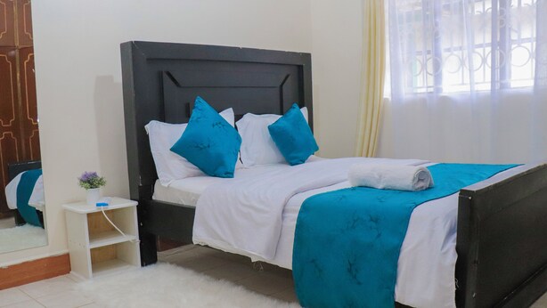 A neatly made bed with white and blue bedding, a small bedside table with a vase, and a white fluffy rug.