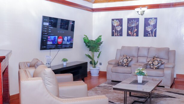 A living room with a beige sofa, a coffee table, a TV mounted on the wall, and a potted plant.