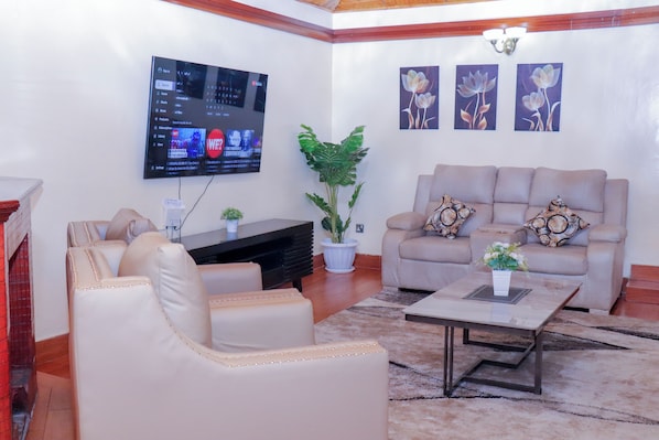 A living room with a beige sofa, a coffee table, a TV mounted on the wall, and a potted plant.