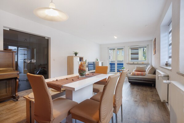A modern living room with a dining table, chairs, a sofa, and a radiator.