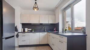 A modern kitchen with light-colored cabinets, a black countertop, and a window with a view of buildings. - Apartment 'Allgäu Space' with Shared Garden, Balcony and Wi-Fi (Marktoberdorf)