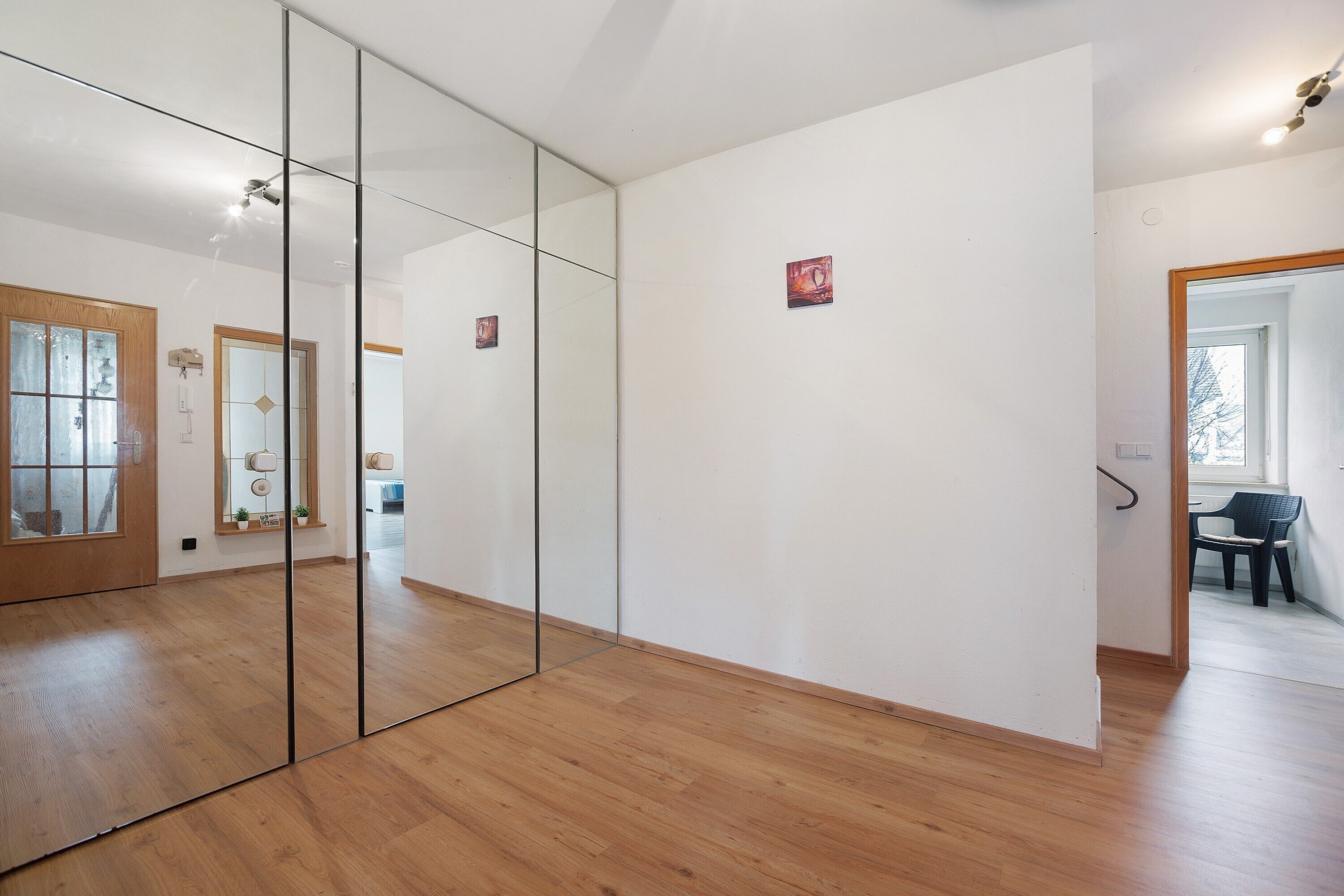 Een kamer met houten vloer, een grote spiegel en een deur naar een andere kamer.